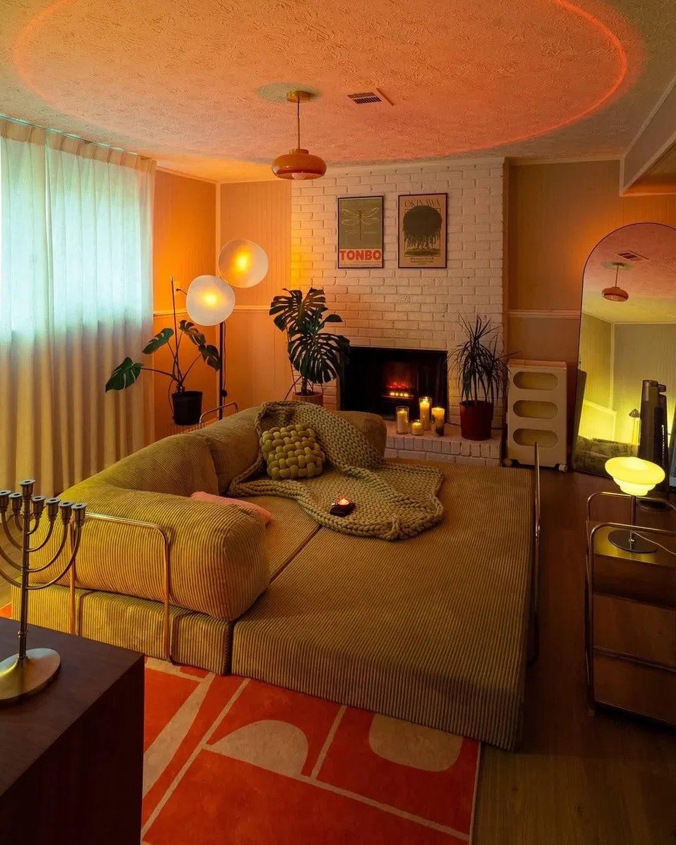 Un salon du soir : canapé en velours côtelé déplié, lampes orange, tapis graphique